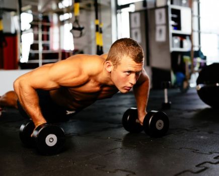 Young man doing pushups while holding dumbbells