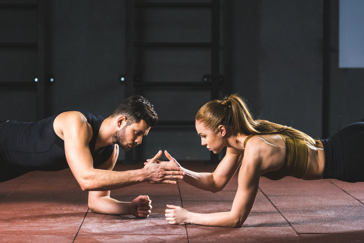 Young athletes giving high five to each other while doing push ups in sports hall