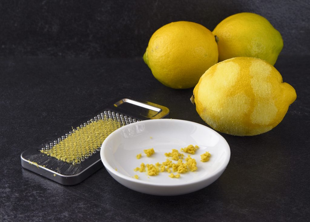 organic lemon fruit, freshly grated peel or rind and the metal grater on a dark slate background with copy space